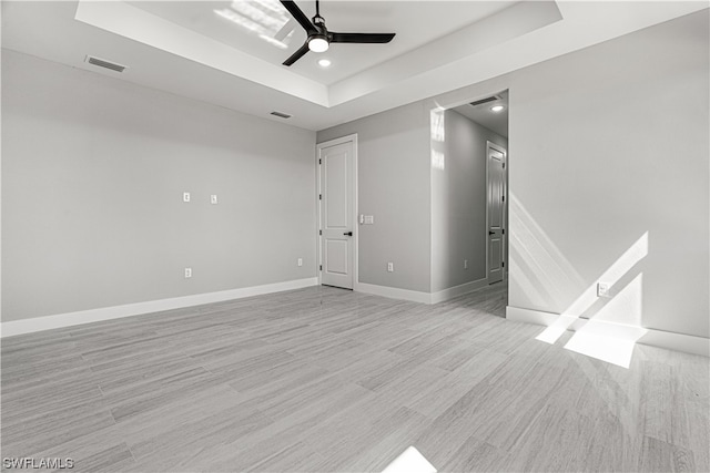 unfurnished room featuring light hardwood / wood-style flooring, a tray ceiling, and ceiling fan