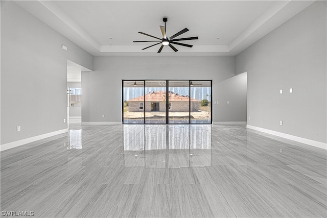 unfurnished living room with ceiling fan, light wood-type flooring, and a raised ceiling