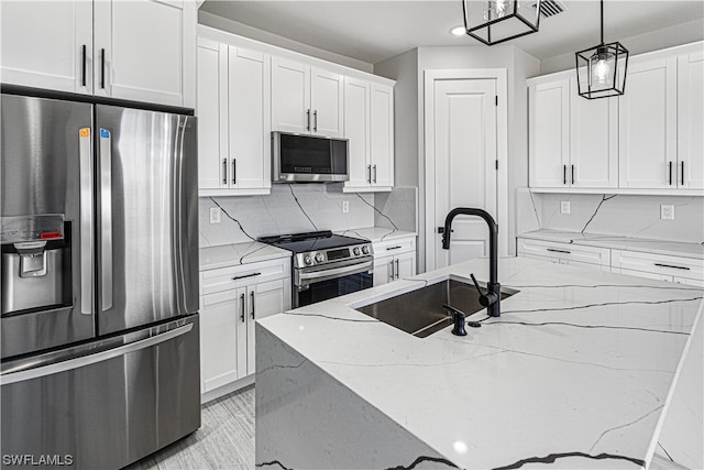 kitchen featuring light stone counters, white cabinets, hanging light fixtures, a center island with sink, and appliances with stainless steel finishes