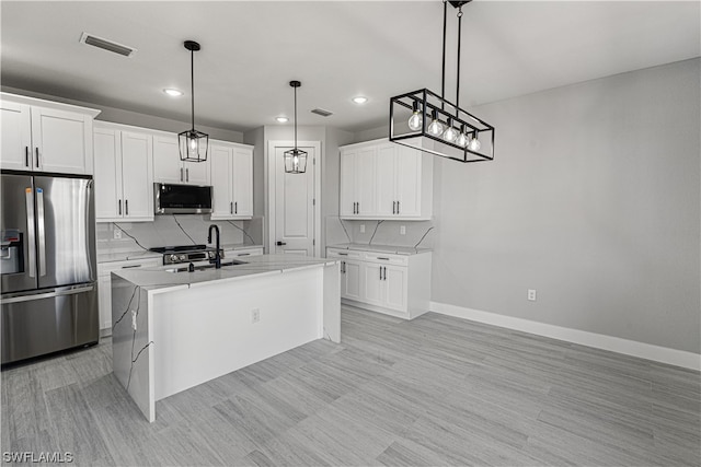 kitchen featuring an island with sink, white cabinets, stainless steel appliances, decorative light fixtures, and sink