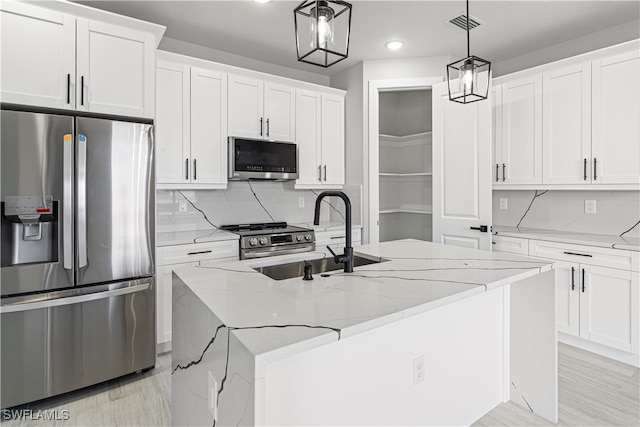 kitchen with sink, white cabinets, stainless steel appliances, a center island with sink, and decorative light fixtures