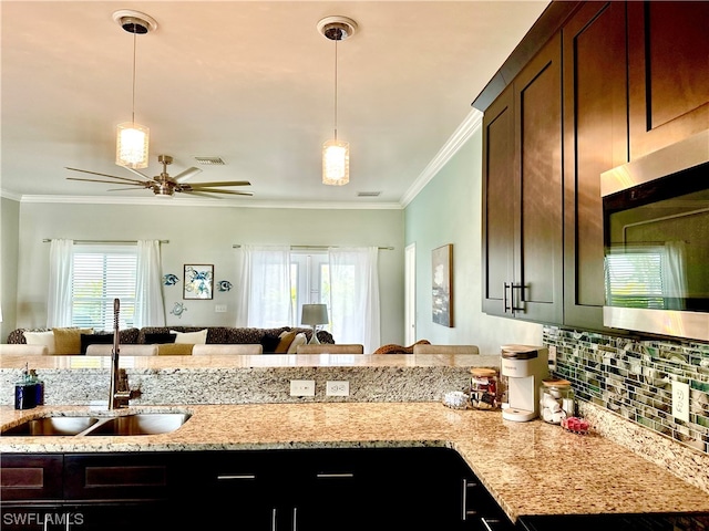 kitchen featuring decorative light fixtures, ceiling fan, ornamental molding, sink, and light stone counters