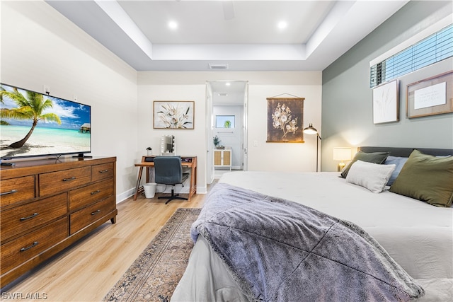 bedroom with a tray ceiling, connected bathroom, ceiling fan, and light wood-type flooring