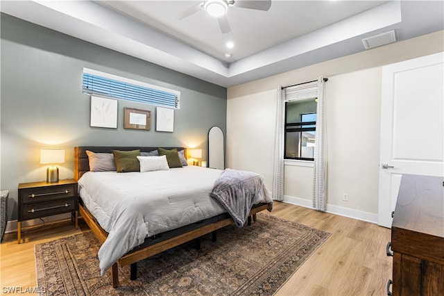 bedroom featuring a raised ceiling, ceiling fan, and light hardwood / wood-style flooring