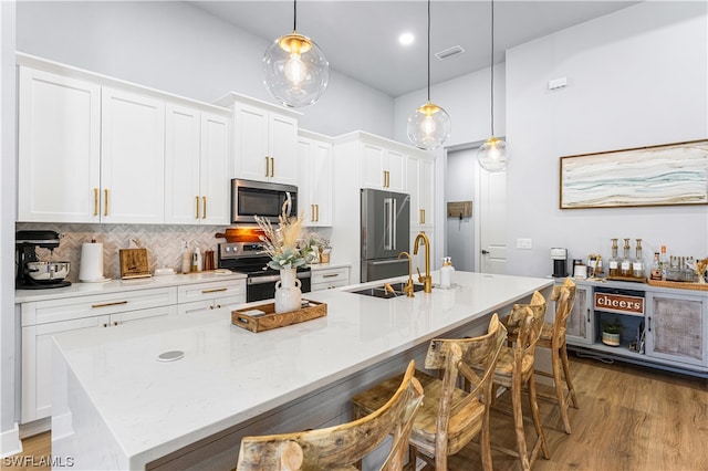 kitchen with a center island with sink, decorative light fixtures, white cabinets, and appliances with stainless steel finishes