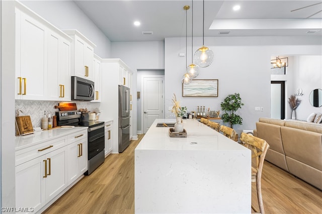 kitchen featuring pendant lighting, stainless steel appliances, light hardwood / wood-style flooring, a breakfast bar area, and white cabinetry