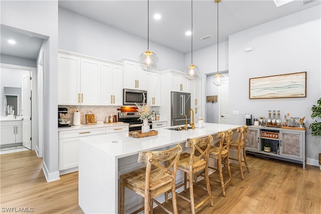 kitchen featuring hanging light fixtures, white cabinets, light hardwood / wood-style floors, stainless steel appliances, and tasteful backsplash