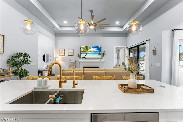 kitchen featuring a raised ceiling, ceiling fan, pendant lighting, and light stone countertops