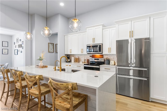 kitchen featuring a kitchen island with sink, pendant lighting, appliances with stainless steel finishes, backsplash, and light wood-type flooring