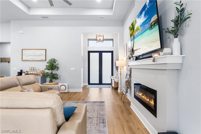 living room with a tray ceiling, light hardwood / wood-style floors, and ceiling fan with notable chandelier