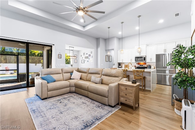 living room featuring sink, ceiling fan, a towering ceiling, light hardwood / wood-style flooring, and a tray ceiling