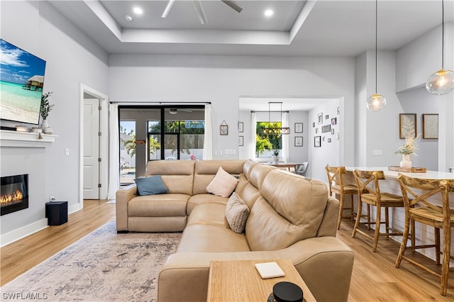 living room with a raised ceiling, ceiling fan, and light wood-type flooring