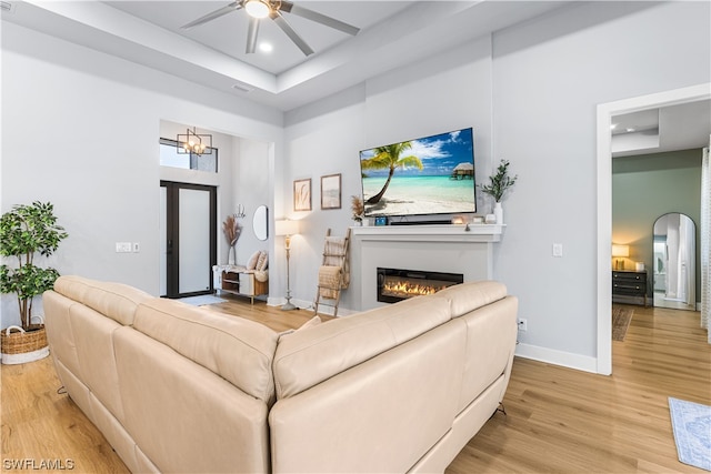 living room with ceiling fan with notable chandelier, a towering ceiling, and light wood-type flooring