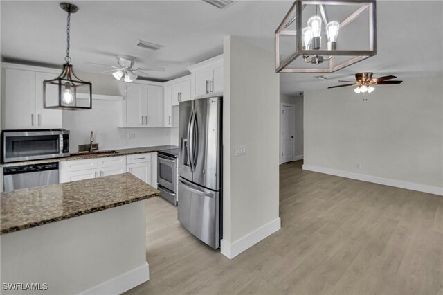 kitchen with pendant lighting, appliances with stainless steel finishes, white cabinetry, dark stone counters, and sink