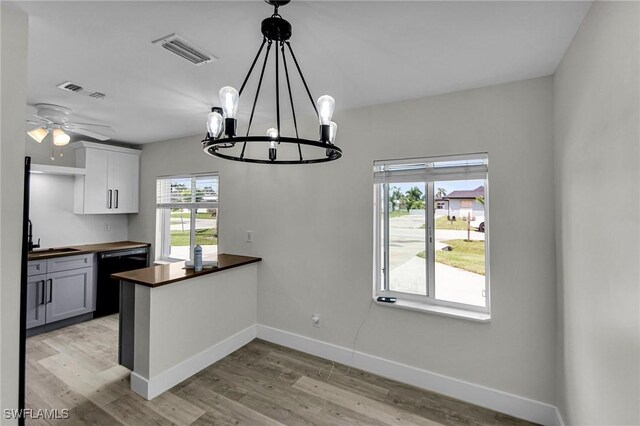 kitchen featuring butcher block counters, black dishwasher, light hardwood / wood-style floors, hanging light fixtures, and white cabinets