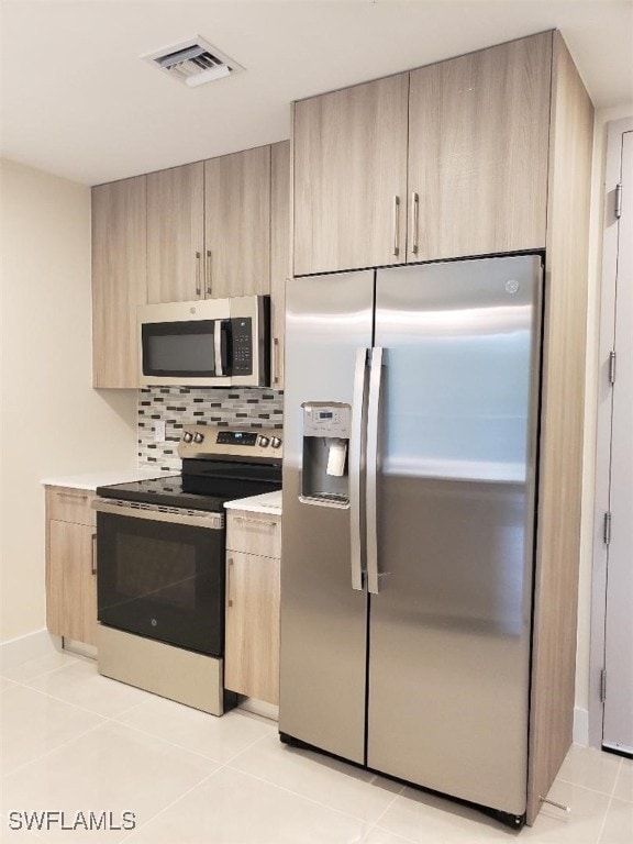 kitchen featuring appliances with stainless steel finishes, light tile patterned floors, decorative backsplash, and light brown cabinets