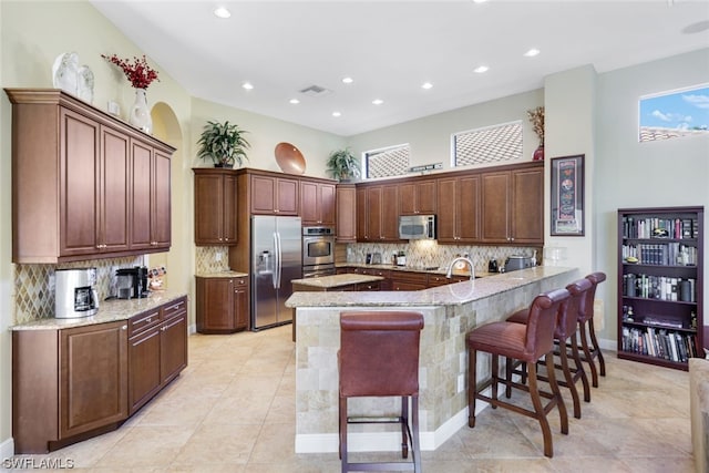 kitchen featuring a kitchen breakfast bar, stainless steel appliances, light tile floors, light stone counters, and tasteful backsplash