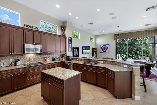 kitchen with ceiling fan, light tile floors, a kitchen island, stainless steel appliances, and light stone countertops