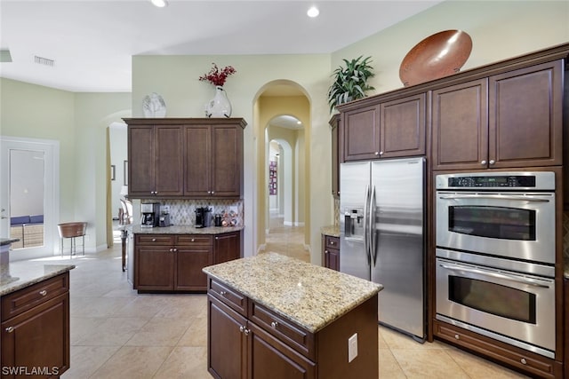 kitchen with light stone countertops, backsplash, appliances with stainless steel finishes, light tile floors, and a center island