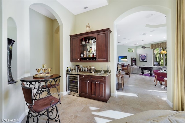 bar with light tile floors, light stone countertops, wine cooler, and ceiling fan