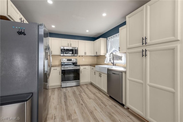 kitchen with sink, white cabinets, stainless steel appliances, and light hardwood / wood-style floors