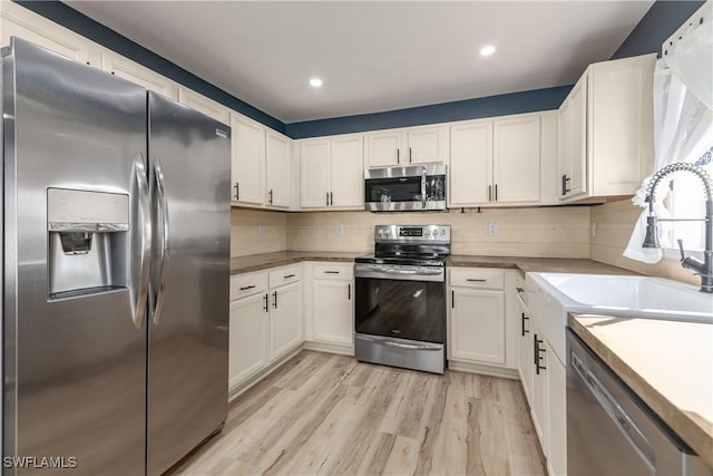 kitchen with white cabinets, sink, decorative backsplash, appliances with stainless steel finishes, and light hardwood / wood-style floors