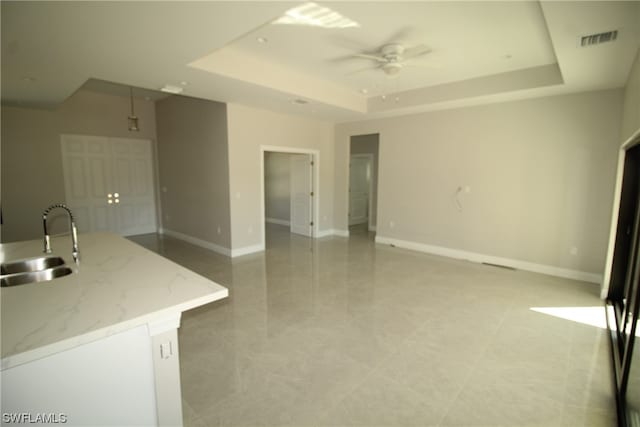 tiled empty room featuring sink, ceiling fan, and a tray ceiling