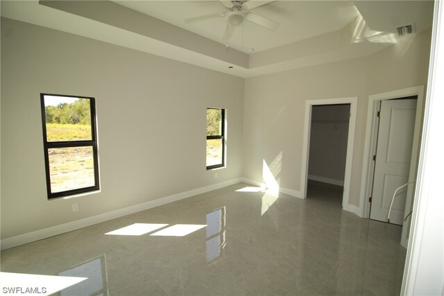 empty room featuring ceiling fan, a raised ceiling, and dark tile flooring