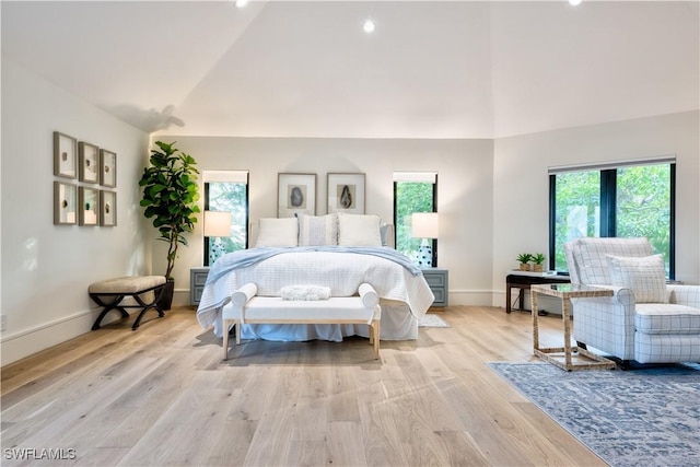 bedroom featuring baseboards, light wood finished floors, and high vaulted ceiling