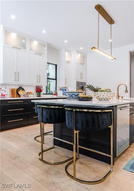 kitchen featuring light countertops, decorative backsplash, dark cabinetry, light wood-style floors, and white cabinetry