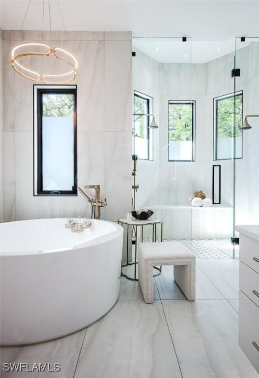full bath with a freestanding bath, tile walls, marble finish floor, a shower with door, and a chandelier