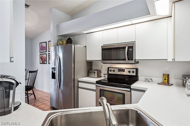 kitchen with lofted ceiling, white cabinetry, appliances with stainless steel finishes, sink, and tile flooring