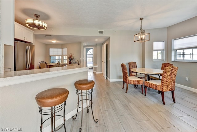 kitchen with pendant lighting, white cabinets, light stone countertops, stainless steel refrigerator, and a breakfast bar area