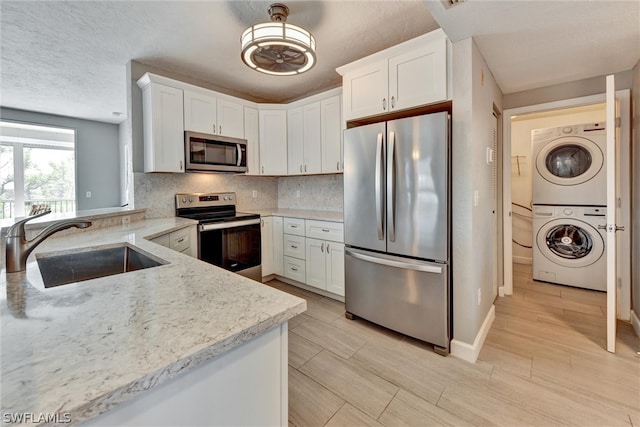 kitchen with white cabinets, stacked washer / drying machine, backsplash, appliances with stainless steel finishes, and sink