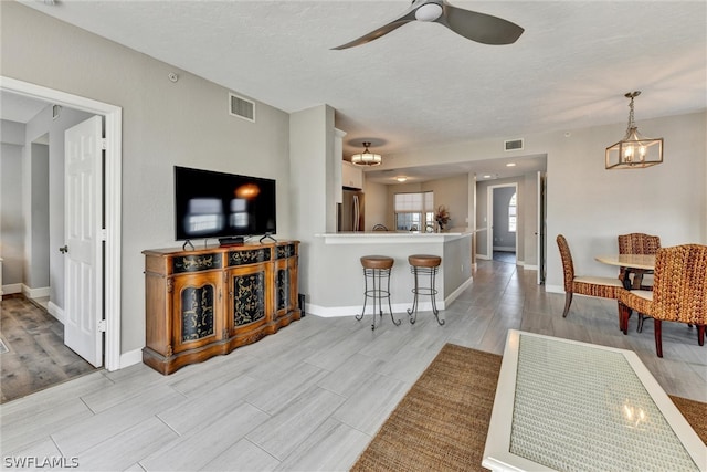 living room with ceiling fan with notable chandelier, a textured ceiling, and light wood-type flooring