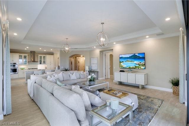 living room with a raised ceiling, an inviting chandelier, and crown molding