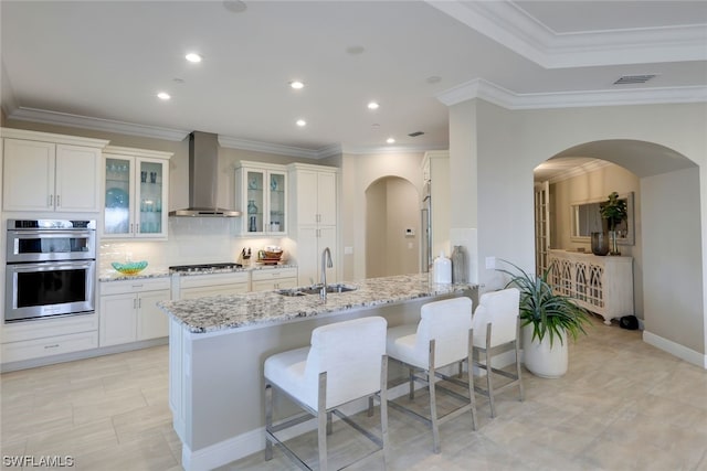 kitchen with wall chimney range hood, white cabinetry, light stone counters, and stainless steel appliances