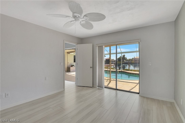 empty room featuring light wood-type flooring, a water view, and ceiling fan