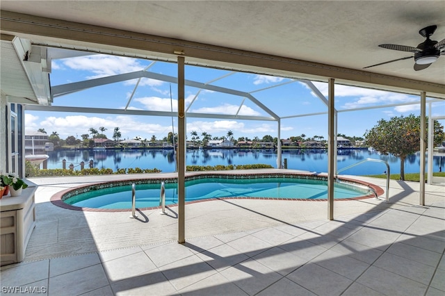 view of swimming pool with glass enclosure, ceiling fan, a water view, and a patio