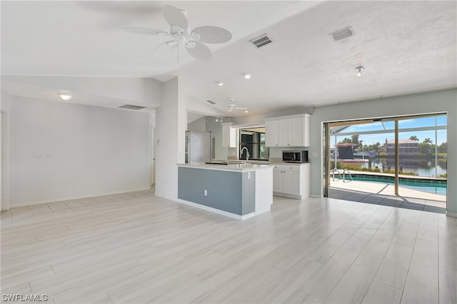 kitchen with a water view, vaulted ceiling, light wood-type flooring, appliances with stainless steel finishes, and white cabinetry