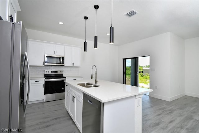 kitchen featuring pendant lighting, white cabinetry, stainless steel appliances, an island with sink, and sink