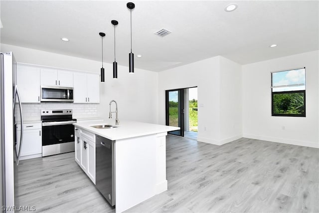 kitchen featuring decorative light fixtures, white cabinetry, stainless steel appliances, sink, and a center island with sink