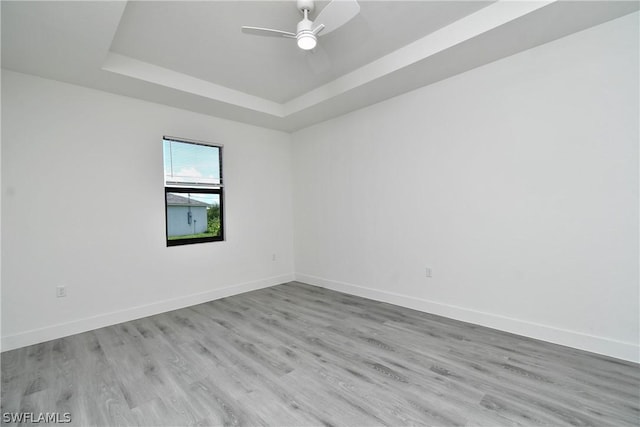 spare room featuring ceiling fan, a tray ceiling, and light hardwood / wood-style flooring