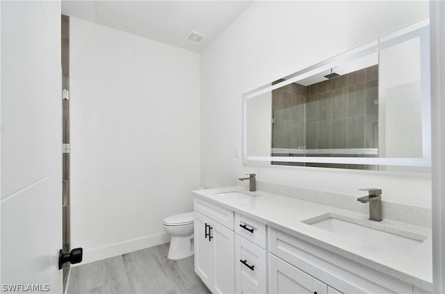 bathroom with hardwood / wood-style flooring, toilet, vanity, and tiled shower