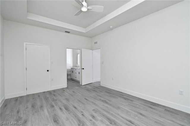 unfurnished bedroom with light wood-type flooring, ceiling fan, connected bathroom, and a raised ceiling