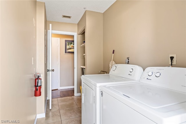 clothes washing area with washer and clothes dryer, a textured ceiling, and light tile floors