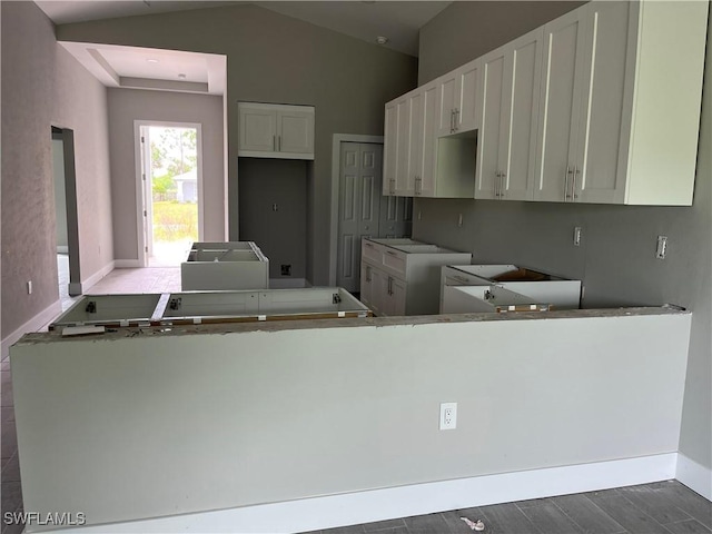 kitchen with kitchen peninsula, white cabinetry, hardwood / wood-style floors, and lofted ceiling