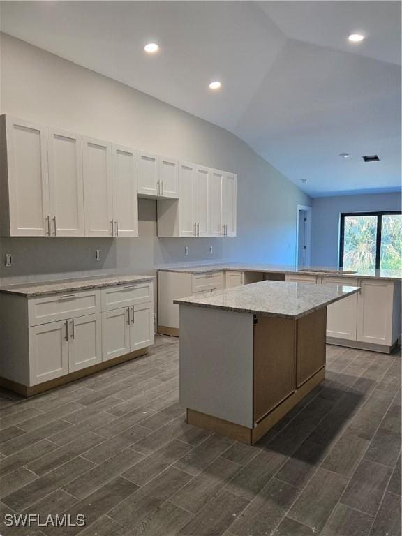 kitchen with a center island, white cabinets, dark wood-type flooring, and vaulted ceiling