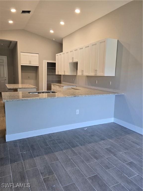 kitchen featuring kitchen peninsula, white cabinetry, vaulted ceiling, and light stone counters