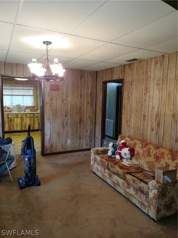 carpeted living room featuring a chandelier, a paneled ceiling, and wood walls